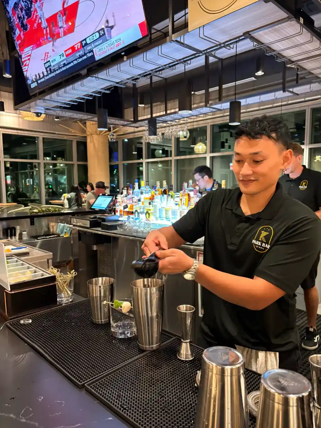 K Park Bar bartender expertly preparing craft cocktails behind the bar wearing branded polo shirt