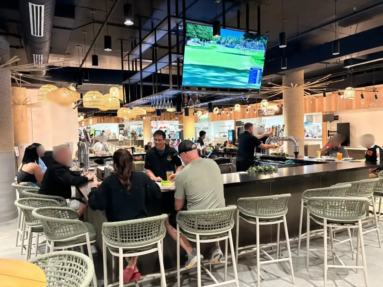K Park Bar interior with customers seated at the bar watching sports on large TVs with tropical rattan seating