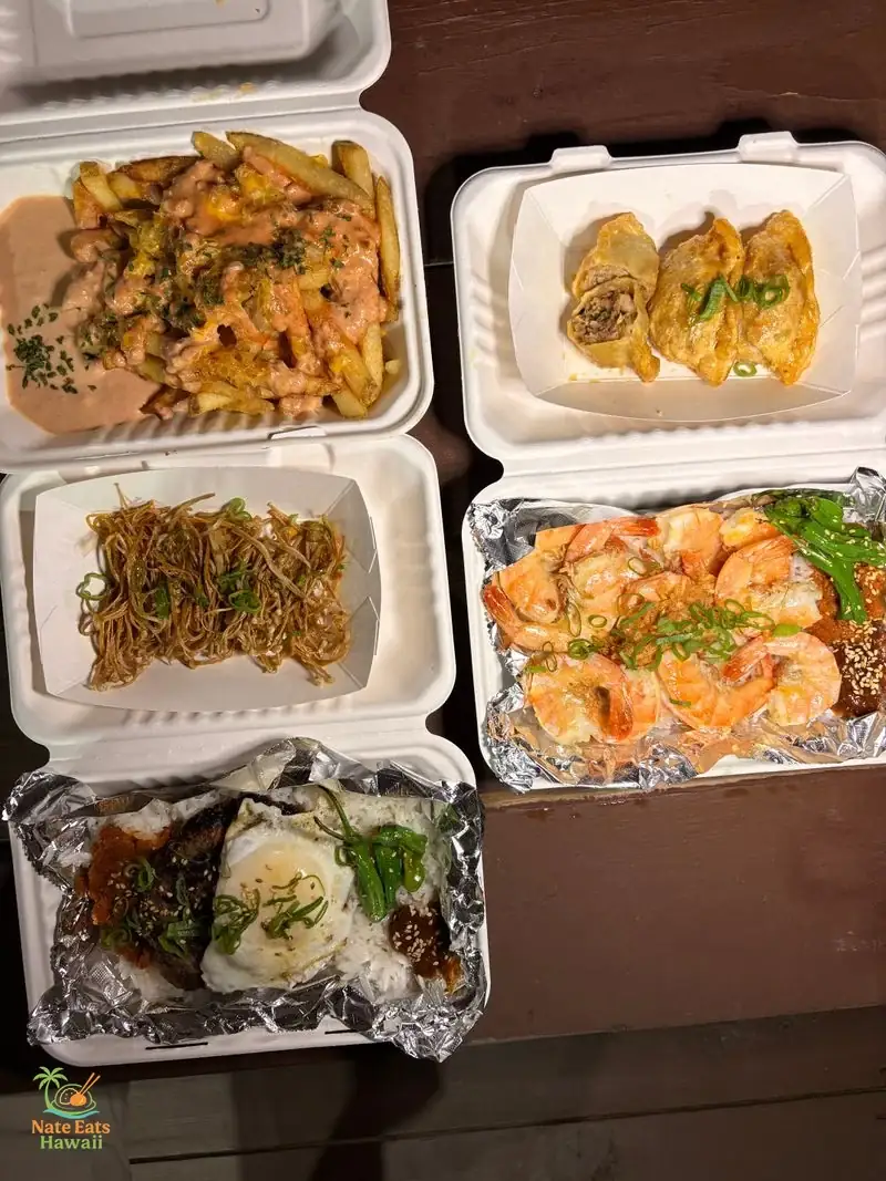 木のピクニックテーブルに並ぶRice & Friesの料理を上から撮影：Animal Style Fries、Fried Mandoo、Fried Enoki Mushrooms、Butter Garlic Shrimp Plate、K-Loco Moco、Steak Plate