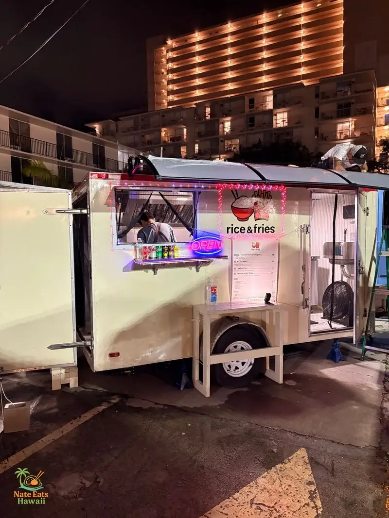 夜のRice & Friesフードトラック外観。白いトラックに赤いロゴ（ライスボウルとフライのバスケット）、ネオンのOPENサイン、メニューボードが映る