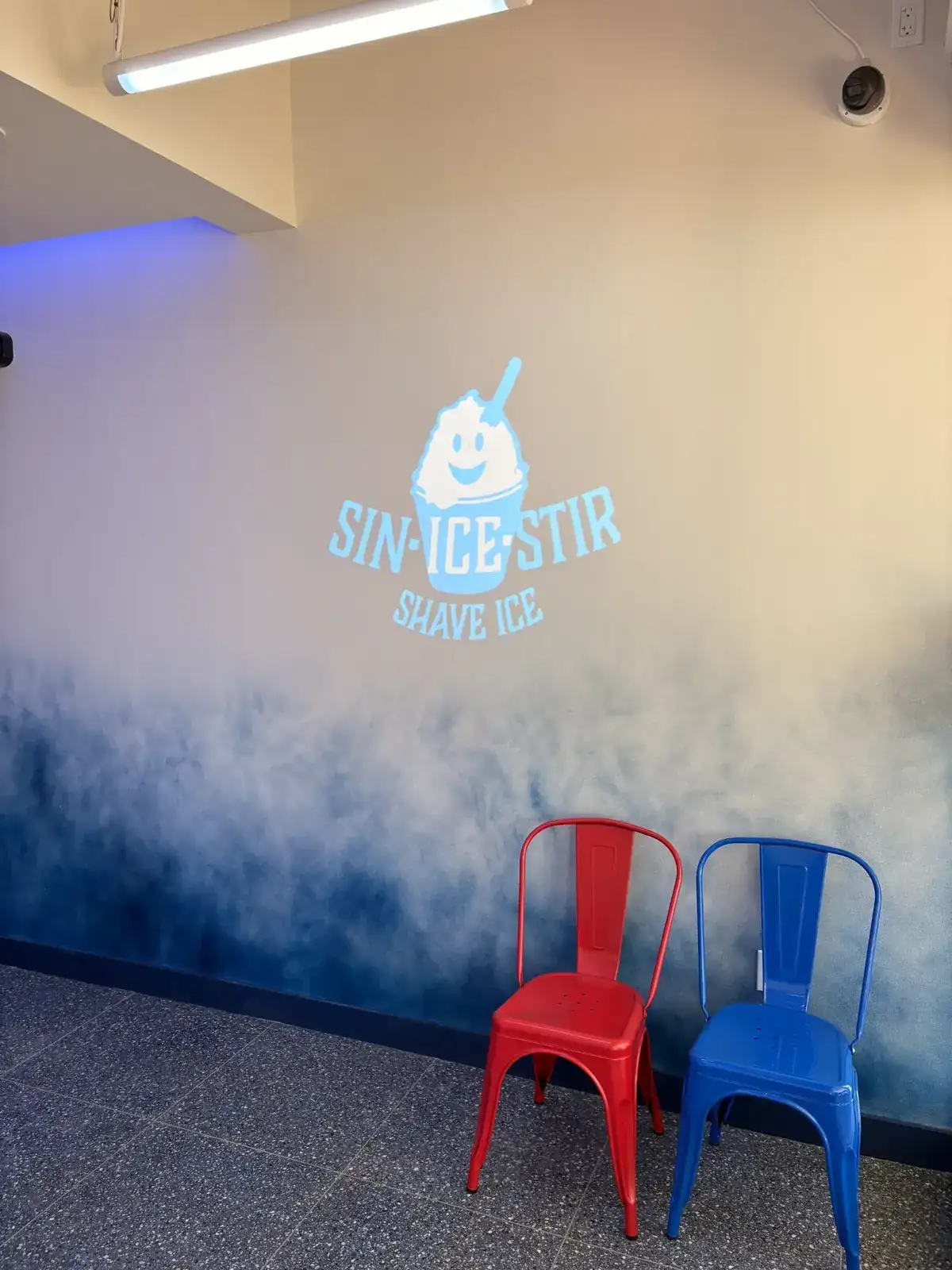 Sin Ice Stir interior showing the Nice logo on gradient blue wall with red and blue metal chairs