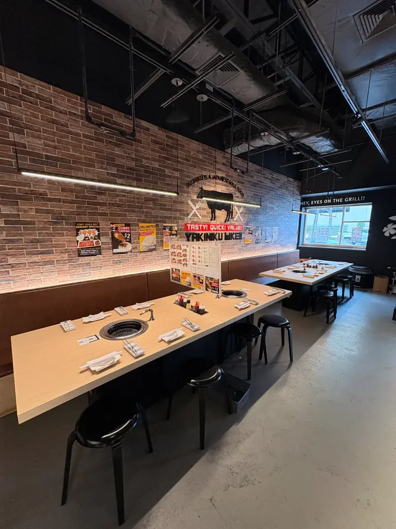 Yakiniku Like Hawaii interior with individual grills at each seat, brick walls, cow illustration, and modern Japanese decor