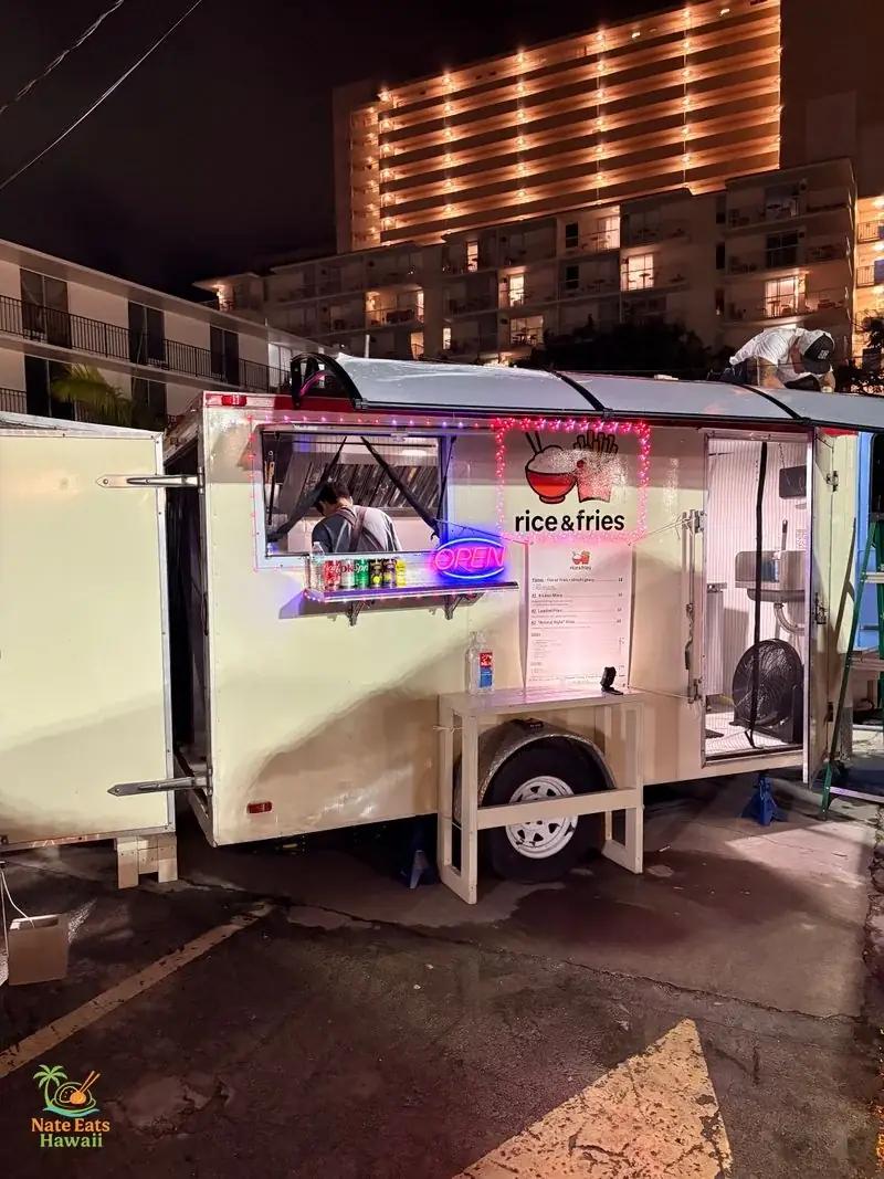 夜のRice & Friesフードトラック外観。白いトラックに赤いロゴ(ライスボウルとフライのバスケット)、ネオンのOPENサイン、メニューボードが映る